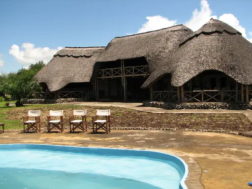 alt="Eco-friendly resort with traditional thatched roofs and a swimming pool, powered by sustainable energy solutions"