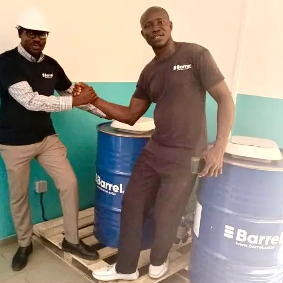 alt="Two men shaking hands next to Barrel solar energy systems in Ivory Coast"