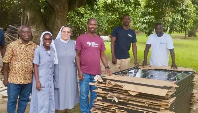 title="Volunteers and nuns collaborating on a solar energy project for rural communities" alt="Group of people, including nuns and volunteers, with solar panels for a sustainable energy project in a rural community"